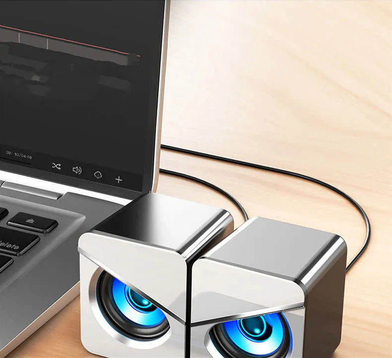 Black and white USB wired mini desktop speaker with volume control next to laptop