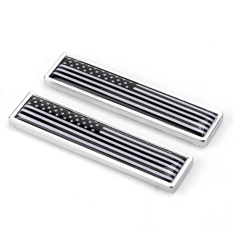 A pair of silver zinc alloy car badge labels with coloured national flag designs, shown at 58mm by 14mm scale.