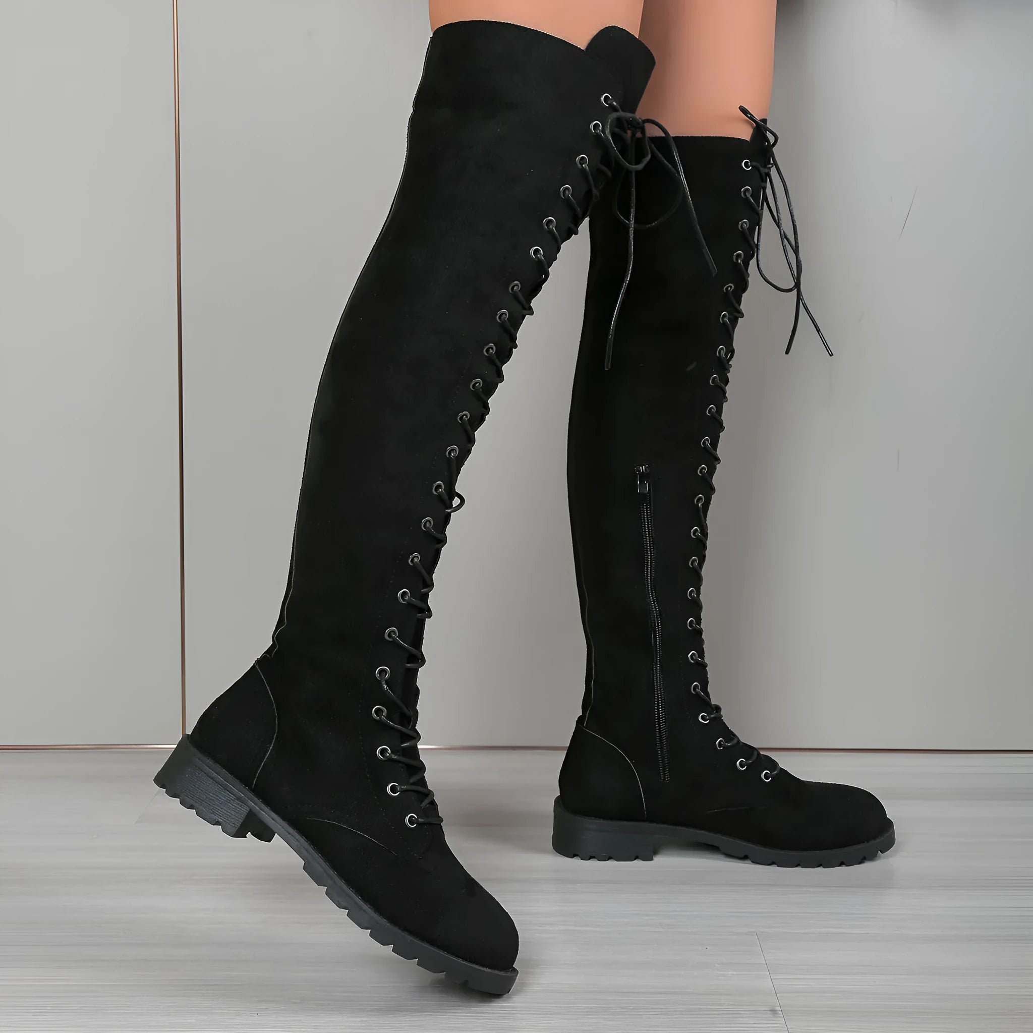 Black lace-up over the knee boots with a round toe and flat rubber sole on a neutral background.