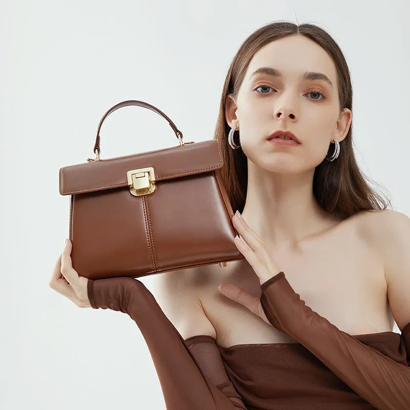 Black leather women's shoulder bag with vachette clasp, shown open to reveal internal zippered pocket.