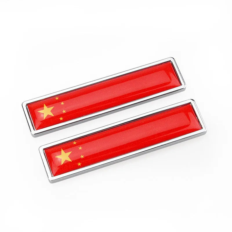 A pair of silver zinc alloy car badge labels with coloured national flag designs, shown at 58mm by 14mm scale.