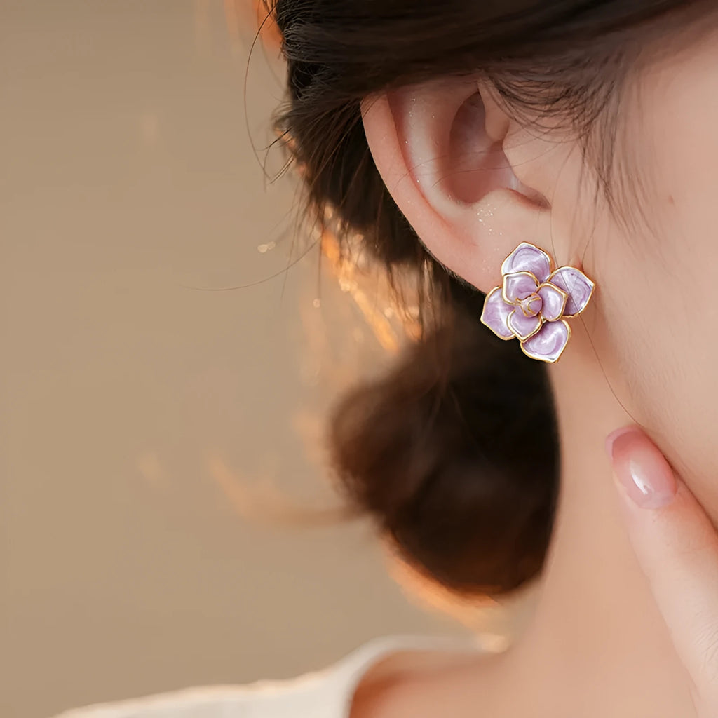 Close-up of a pair of gold plated flower stud earrings with a purple oil-spot glaze finish.