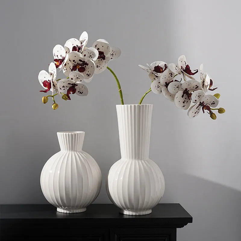 White ceramic ball vase with blue stripes and artificial blue orchid stems on a wooden table.