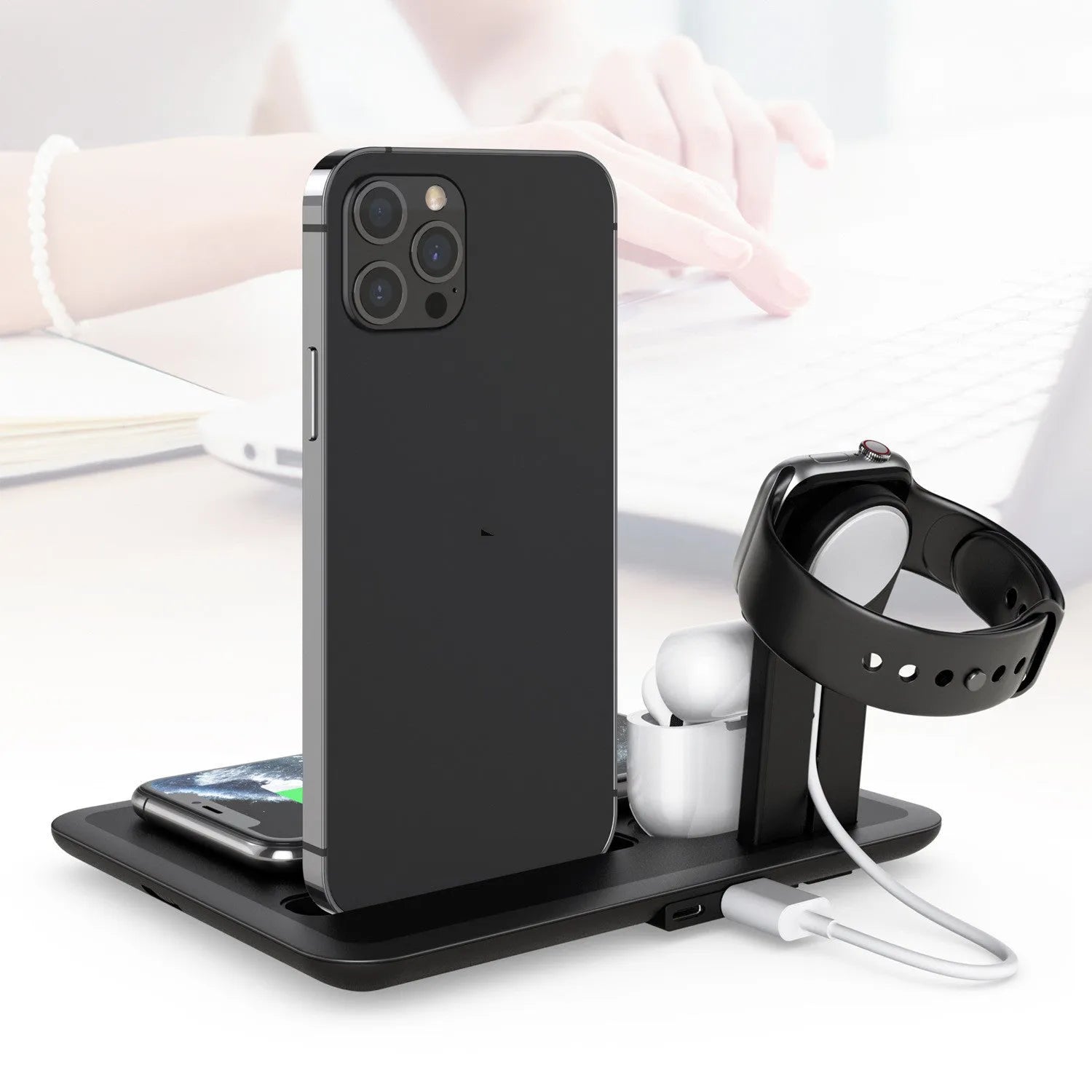 Black desktop wireless charging station with phone on pad, showing watch and headphone charging ports.