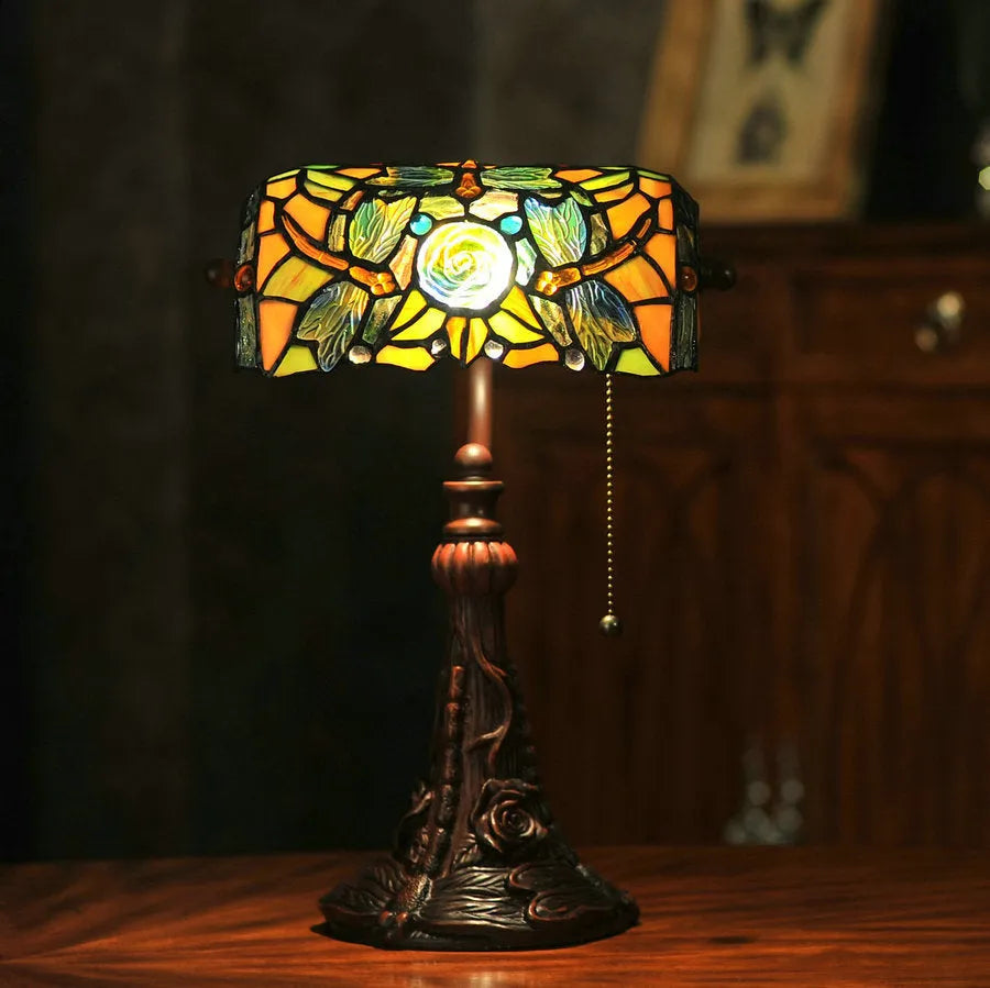 Tiffany stained glass table lamp on a desk, showing its coloured shade and resin base.