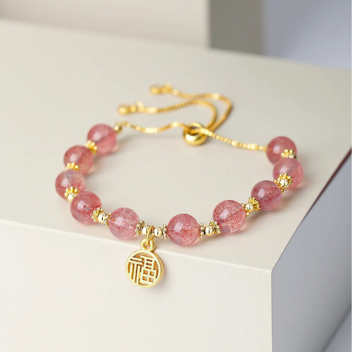 A geometric crystal bracelet in strawberry quartz colour with a fu character detail.