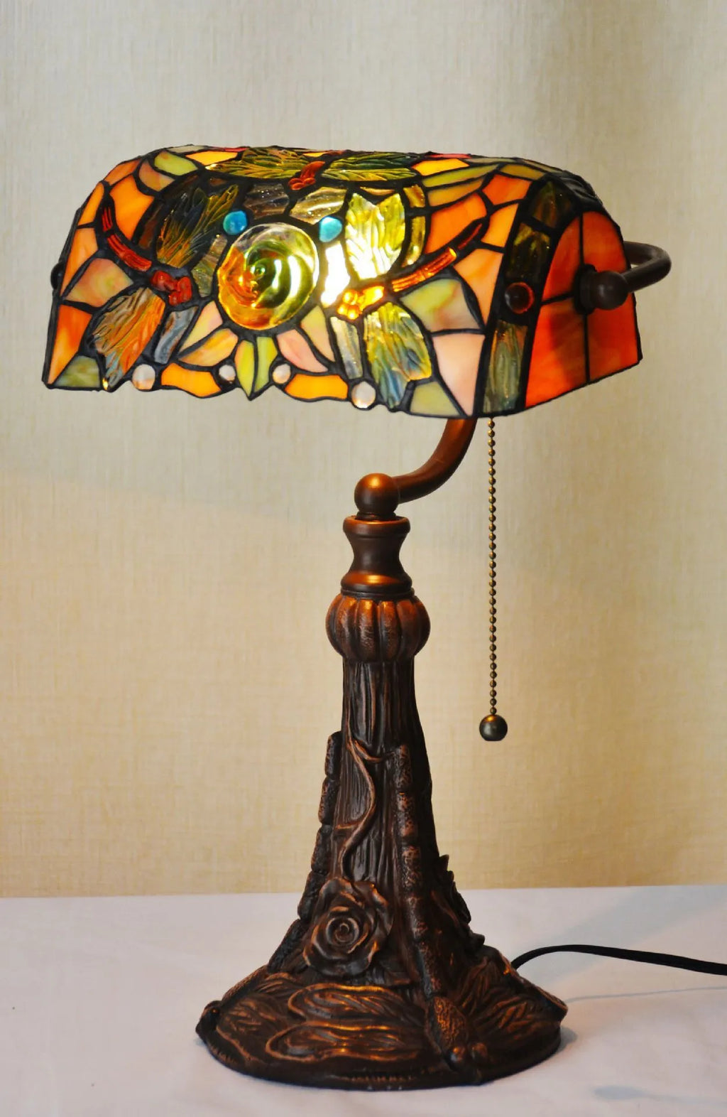 Tiffany stained glass table lamp on a desk, showing its coloured shade and resin base.