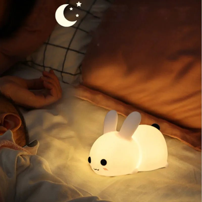 White silicone rabbit night light with warm and white LED glow on a wooden bedside table